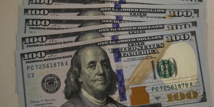 Several overlapping $100 bills fanned out, showing Benjamin Franklin and the blue security stripe.