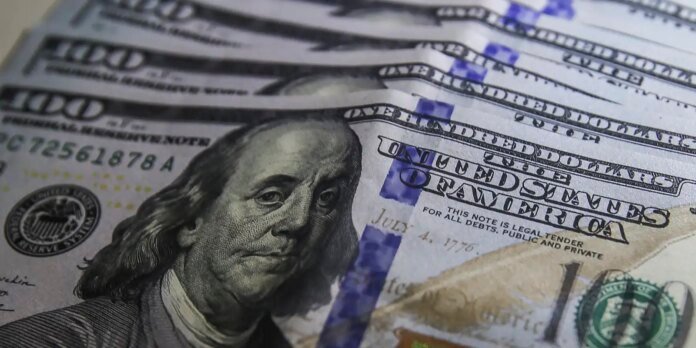Close-up view of multiple US $100 bills, showing Benjamin Franklin's portrait and blue security strip
