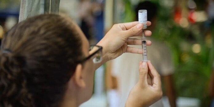 Close-up of hands drawing vaccine from a vial into a syringe, with a blurred background.