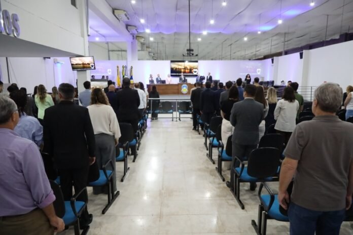 Large conference hall with a panel of speakers at a long desk on a stage, audience standing and facing forward.