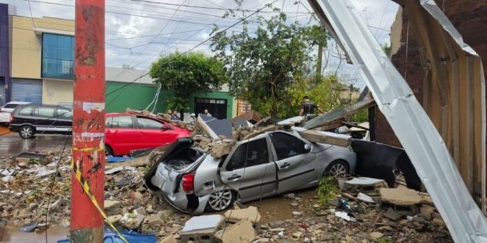 Silver sedan crushed under collapsed roof and concrete debris on a street; bystanders and a red car in the background.
