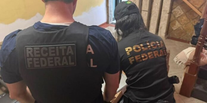 Two federal police officers seen from the back, wearing vests labeled Receita Federal and Polícia Federal in Brazil.