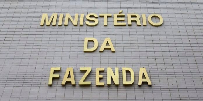 Gold letters spell 'MINISTÉRIO DA FAZENDA' on a gray tiled wall, forming a government sign.