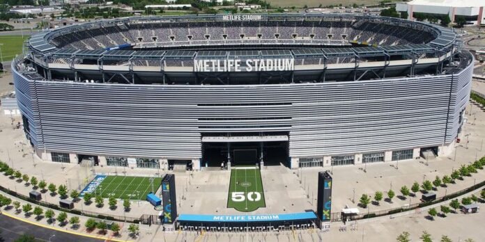 Aerial view of MetLife Stadium with a football field visible in front and seating around the oval stadium, signage reading MetLife Stadium above the entrance.