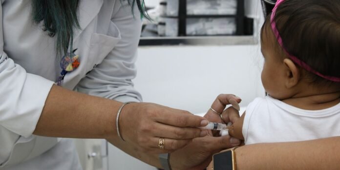 Healthcare worker administers a vaccine to a child, inserting a syringe into the child’s upper arm in a clinical setting.