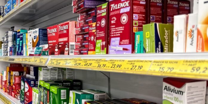 A pharmacy aisle with red Tylenol boxes and various medicines on shelves, yellow price tags along the front edge of the lower shelf.