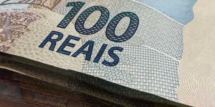 Close-up of a 100 reais banknote showing the blue '100 REAIS' text and detailed security patterns.