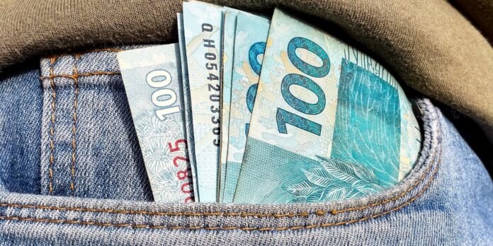 Several blue 100 reais banknotes protrude from the back pocket of blue denim jeans.