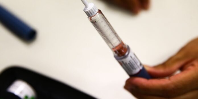 Syringe with liquid vaccine being prepared, held by hands over a blurred background