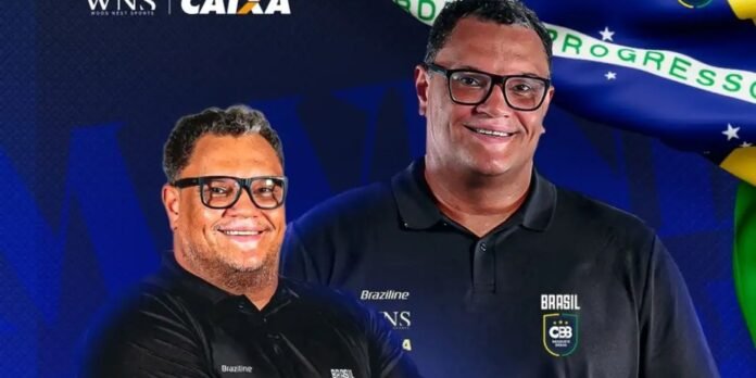 Two smiling men in black polo shirts with Brazil basketball crest, standing together against a blue background with flags behind them.