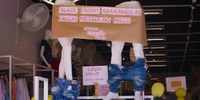 Shop window display with mannequins wearing jeans around their waists; signs in Portuguese advertise Black Friday, 50% off, except new collection (nova).