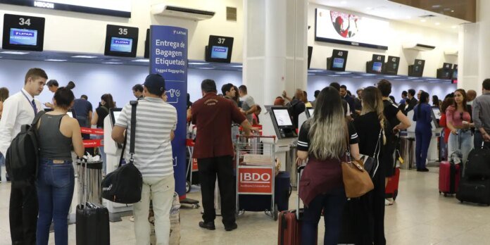 Airport check-in area with passengers queuing and luggage carts under numbered counters 34–45.