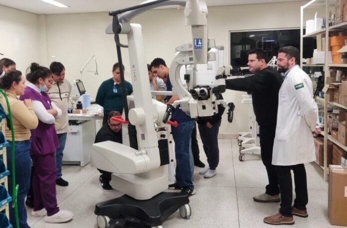 Group of people observing a medical robotic arm demonstration in a lab; a clinician guides the arm while others watch.