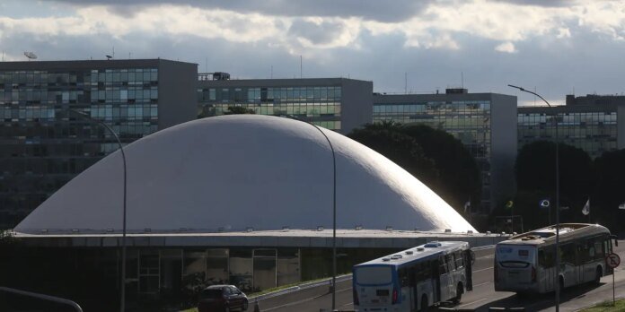 White curved dome building along a road with two buses in the foreground and glass-fronted office blocks behind it.