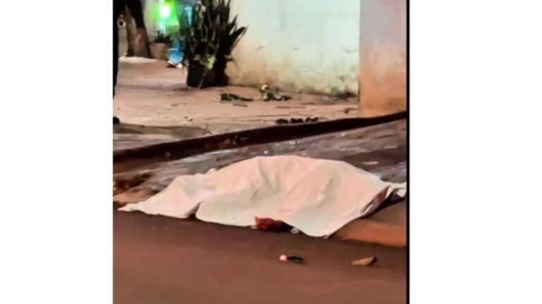 Person covered by a light sheet lying on the street beside a curb at night