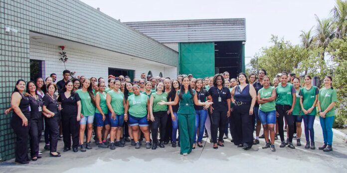 Large diverse group of employees posing for a group photo outside a building, many in green shirts, smiling at the camera.