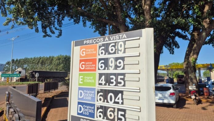 Fuel price board at a roadside station showing numbers like 6,69; 6,99; 4,35 etc. with a blue sky behind and trees nearby (informative image).