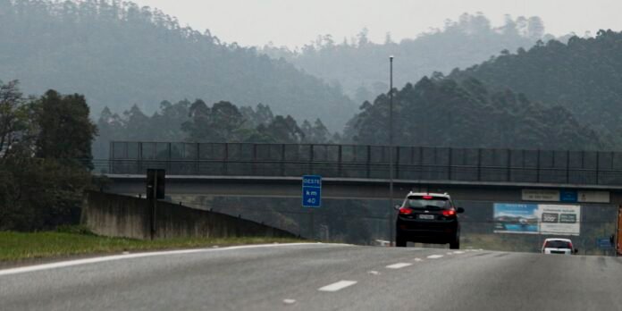 Two-lane road with an overpass, blue km 40 Oeste sign, and cars driving toward the horizon against a misty hillside backdrop.