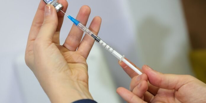 Person drawing liquid from a vial into a syringe, preparing an injection.