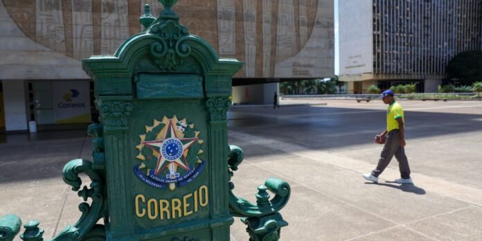 Ornate green Brazilian mailbox with the coat of arms and the word CORREIO, set in a paved plaza with a man in a bright yellow shirt walking in the background.