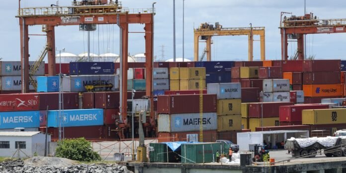 Busy container port with stacked shipping containers and large cranes overhead, cargo yard in use at a dockyard site