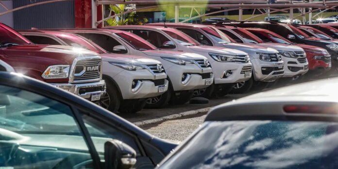 Row of red and white pickup trucks parked side by side at a car dealership lot for sale.