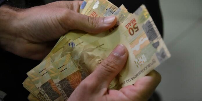 Hands counting a stack of 50 reais banknotes