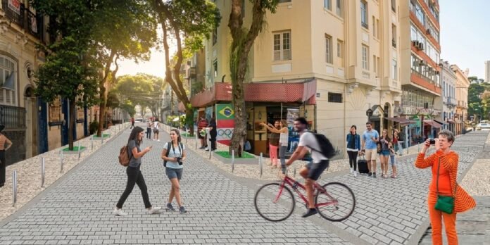 Pedestrian street scene with people walking, a cyclist in motion, and a woman in orange taking a photo; buildings line a sunny, cobbled avenue and a Brazilian flag mural is visible on a storefront.