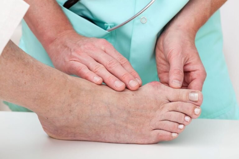 Podiatrist examining a patient's bare foot, hands on the foot during a medical checkup in teal scrubs.