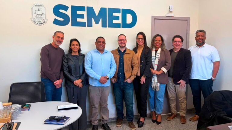Group of nine professionals standing side by side in front of a wall with the SEMED logo, posing for a team photo in an office conference area.