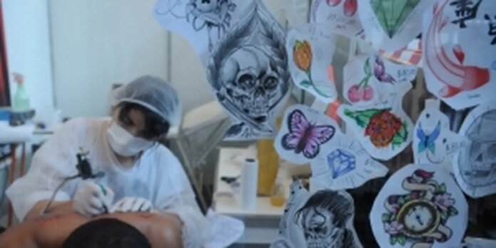 A healthcare worker in a mask and cap performing a procedure on a patient in a clinical room, with colorful drawings taped to the wall nearby.