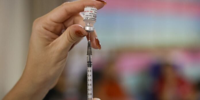 Close-up of a hand drawing liquid from a vaccine vial into a syringe, ready for injection.