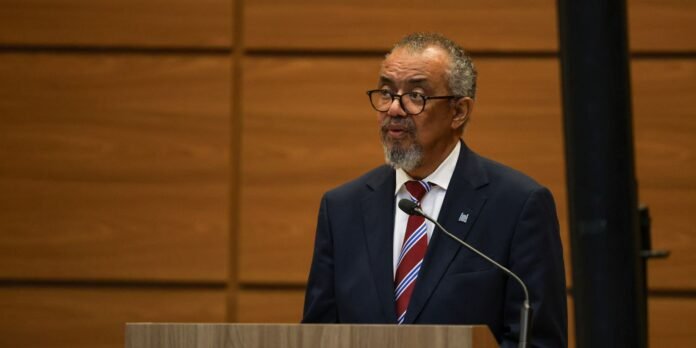 Man in a dark suit and red striped tie speaking at a wooden podium with a microphone.