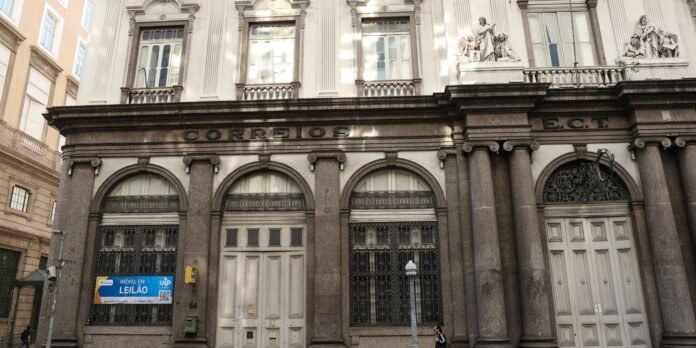 Historic postal building with stone arches and tall columns; ornate façade and statues on upper level; a blue