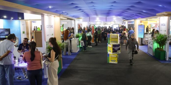 Crowded trade show hall with colorful booths and attendees exploring displays under a blue ceiling.