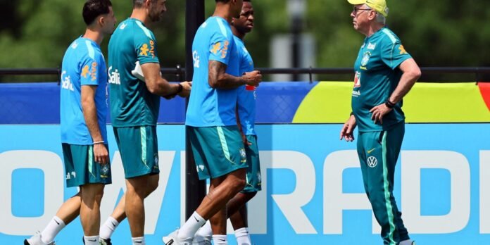 Coach in a yellow cap talks to four players in teal and blue training outfits on a sunny practice field with a large blue advertising banner nearby.