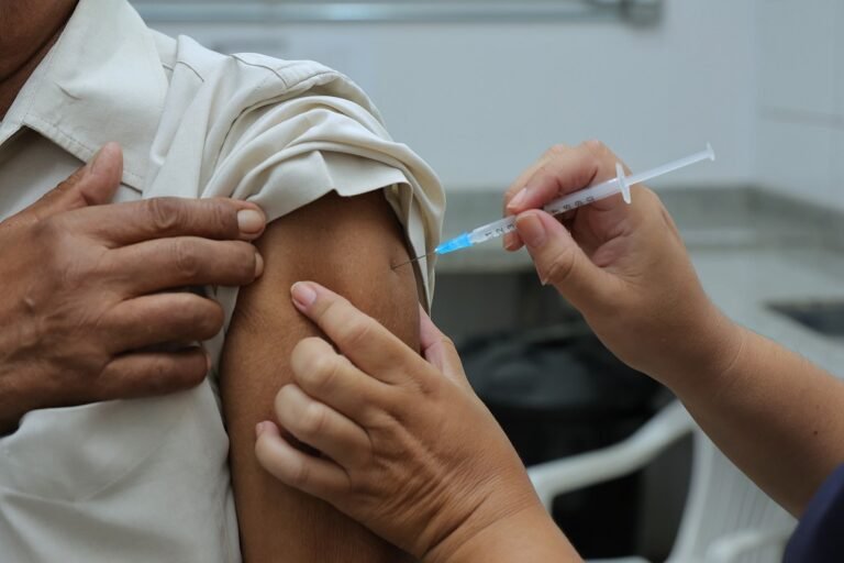 Medical professional administers a vaccine shot to a patient's upper arm with a syringe and needle visible