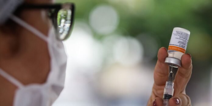 Healthcare worker wearing a mask and goggles draws vaccine into a syringe from a small vial outdoors.