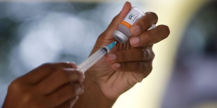 Close-up of hands drawing liquid from a vaccine vial into a syringe for vaccination.