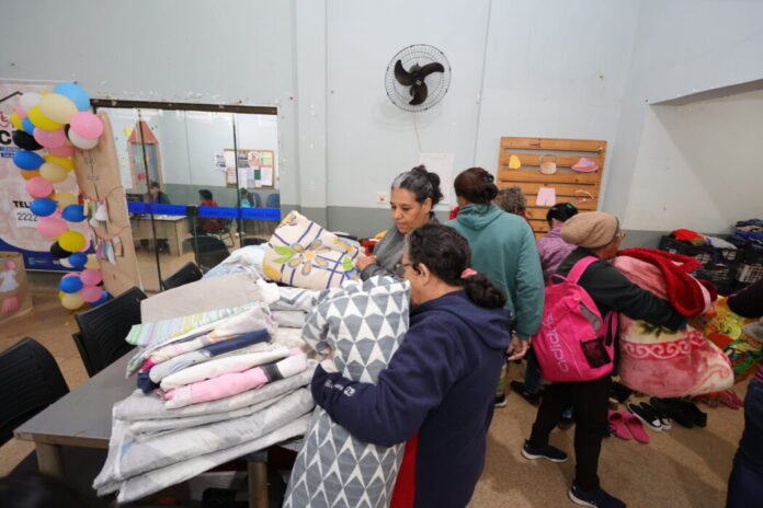 People in a donation center sorting and selecting blankets from a table of folded quilts and pillows.