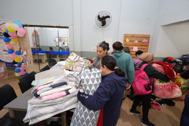 People in a donation center sorting and selecting blankets from a table of folded quilts and pillows.