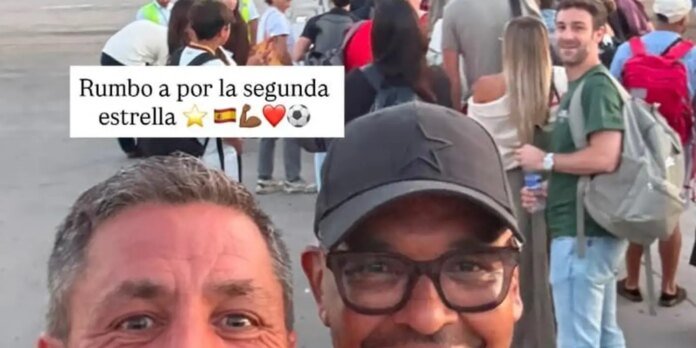 Two men take a selfie in a crowded outdoor area; caption overlay reads 'Rumbo a por la segunda estrella' with a star, Spain flag, flexed biceps, heart, and soccer ball emojis.