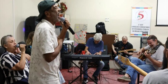 Group of seniors performing music in a community room: a man sings into a microphone while others play keyboard and guitars.