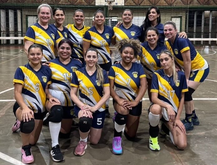 Twelve female volleyball players in matching yellow and navy uniforms pose on an indoor court, kneeling in front and standing behind, smiling for a team photo.