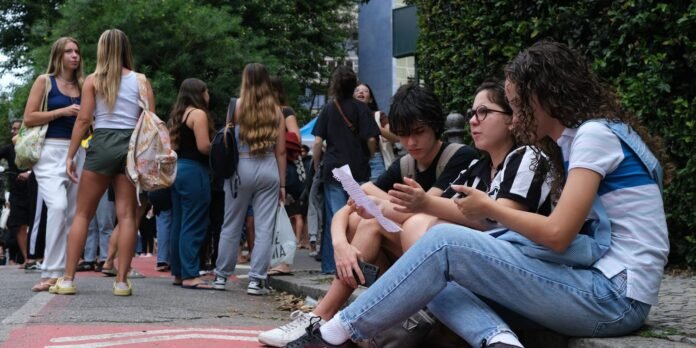 Group of students outdoors with backpacks, standing and talking along a sidewalk near greenery.
