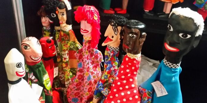 Row of handmade cloth puppets with exaggerated faces wearing bright patterned clothing on a shelf.