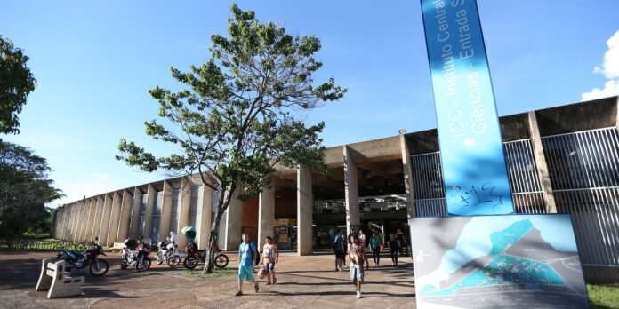 Blue vertical banner reading 'ICC - Instituto Central de Ciencias - Entrada' in front of a concrete campus building; people walk past parked motorcycles and a map sign nearby.