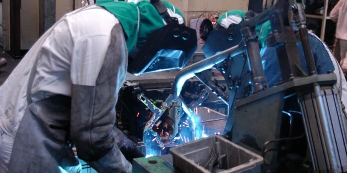 Welders in protective gear welding metal with bright sparks flying in a workshop.