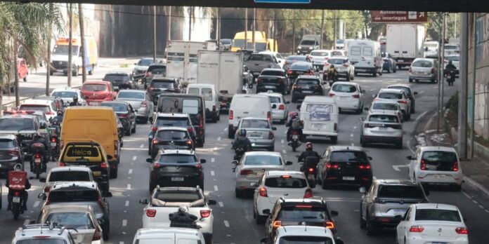 Busy urban street with multiple lanes of cars, vans, and motorcycles in heavy traffic during daytime.