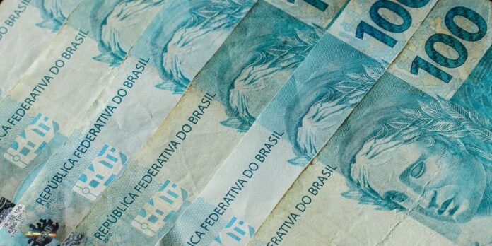 Close-up of blue 100 reais banknotes fanned in a stack, showing 'República Federativa do Brasil'.